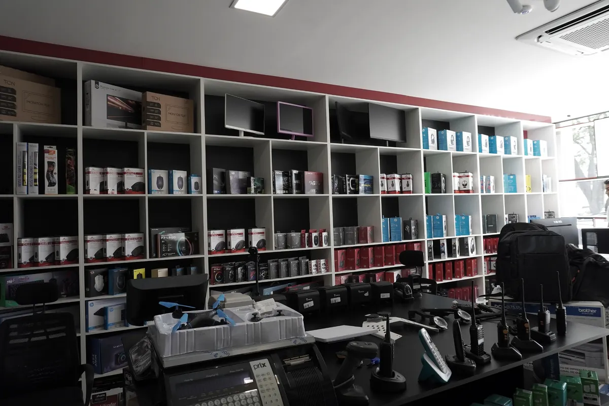 Parede de prateleiras com produtos de informática, monitores e balcão de atendimento da Barbosa Informática