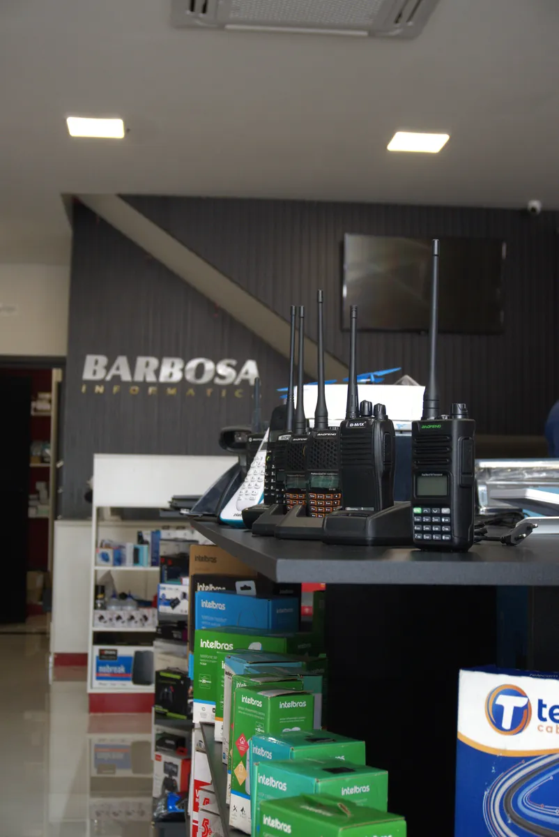 Rádios comunicadores no balcão, com o letreiro da Barbosa Informática ao fundo