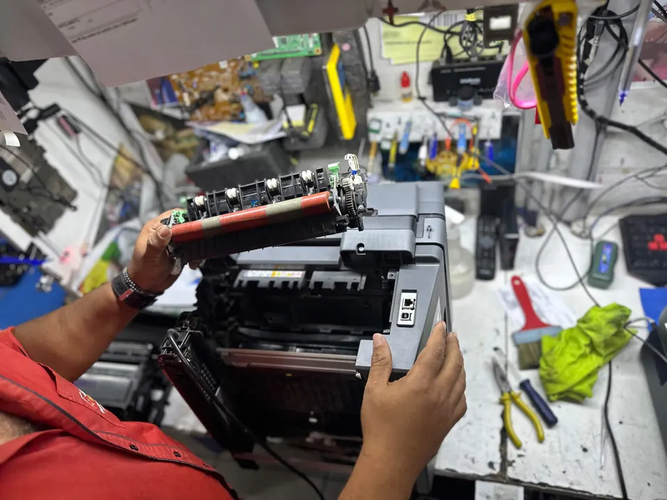 Técnico trocando peça de uma impressora na bancada
